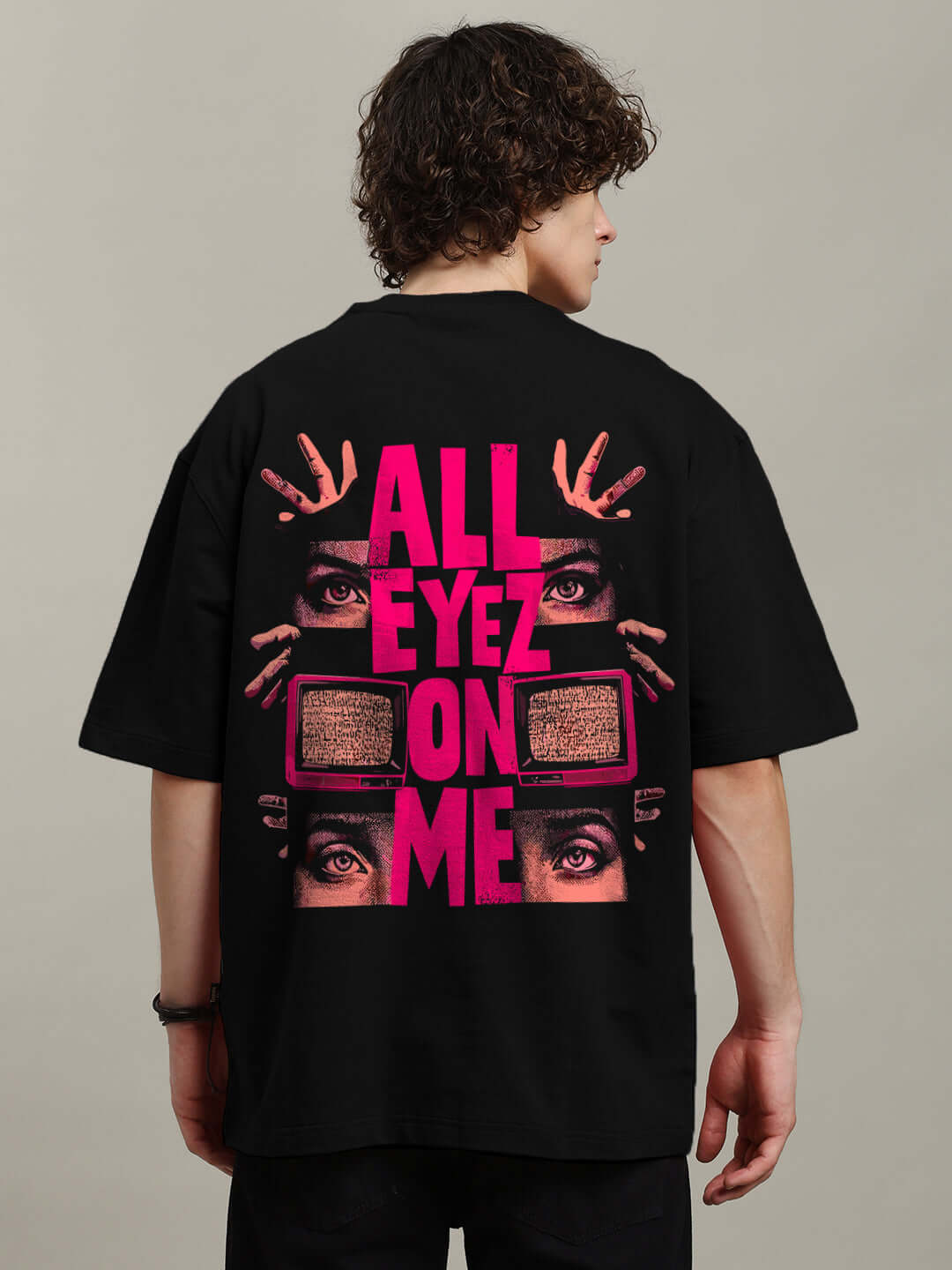 Model wearing black oversized t-shirt with bold 'All Eyez On Me' graphic in pink and black, made of premium cotton blend. Eyecatching design.