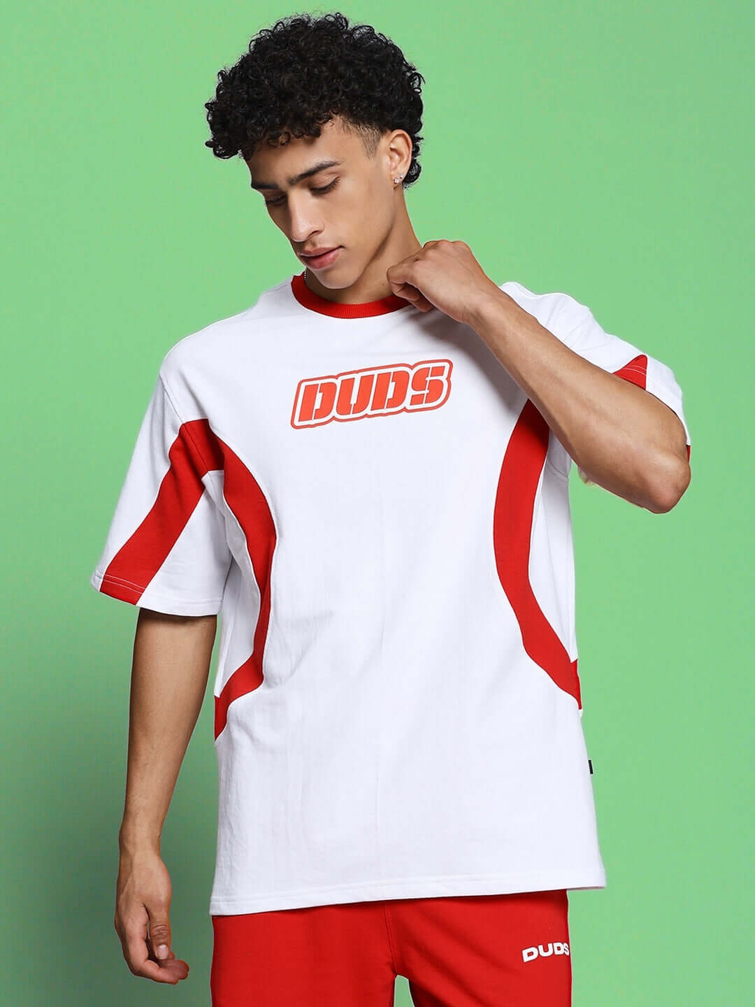 Man wearing EZEL OVER-SIZED T-SHIRT WHITE RED with bold streetwear style in premium cotton, set against a green background.