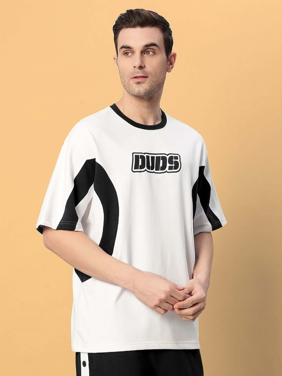 Model wearing EZEL OVER-SIZED T-SHIRT BLACK WHITE, standing against peach background, showcasing streetwear fashion.