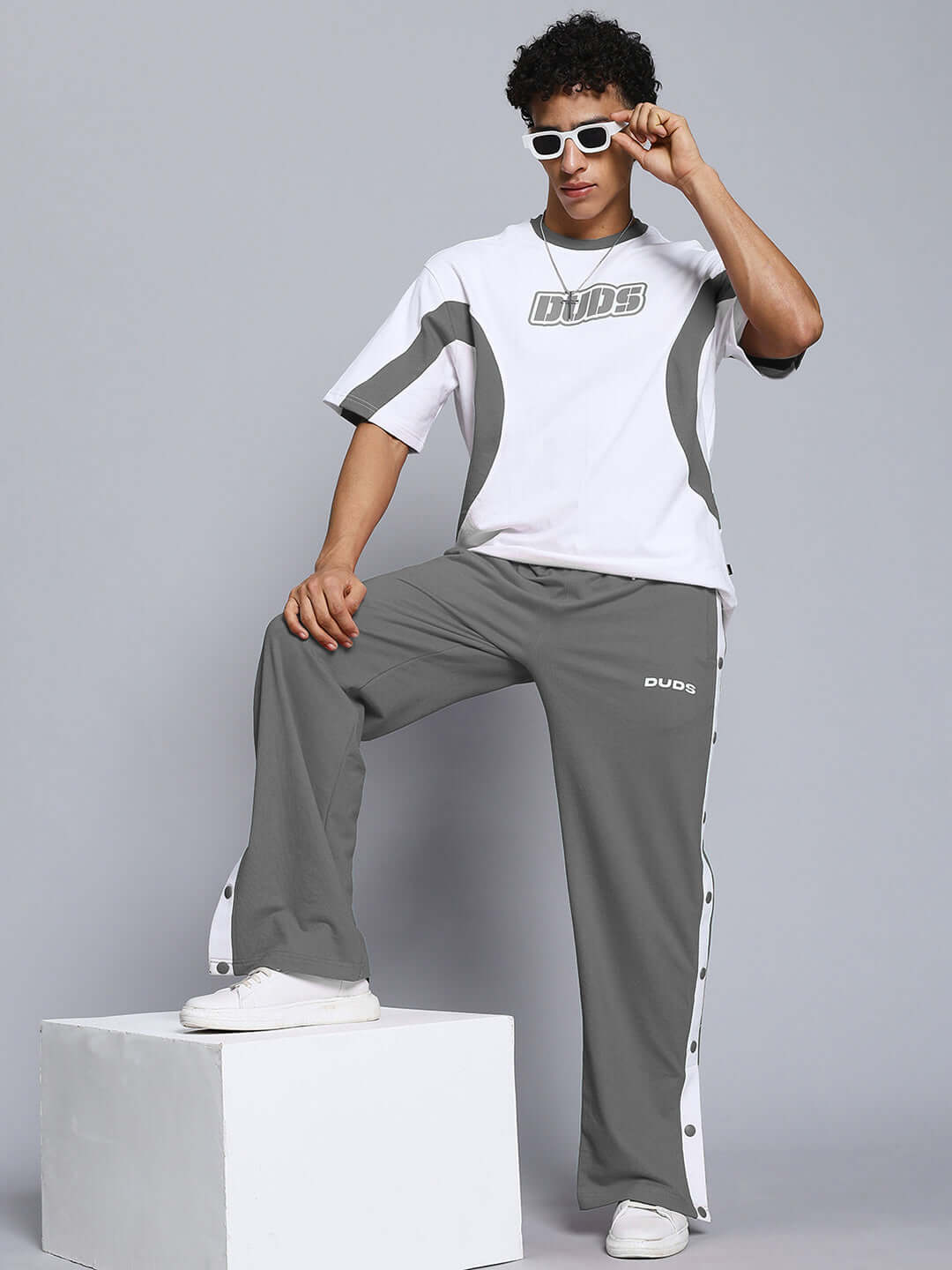 Model wearing EZEL relaxed fit white-grey co-ord set with contrast panel joggers and sunglasses, unisex design.