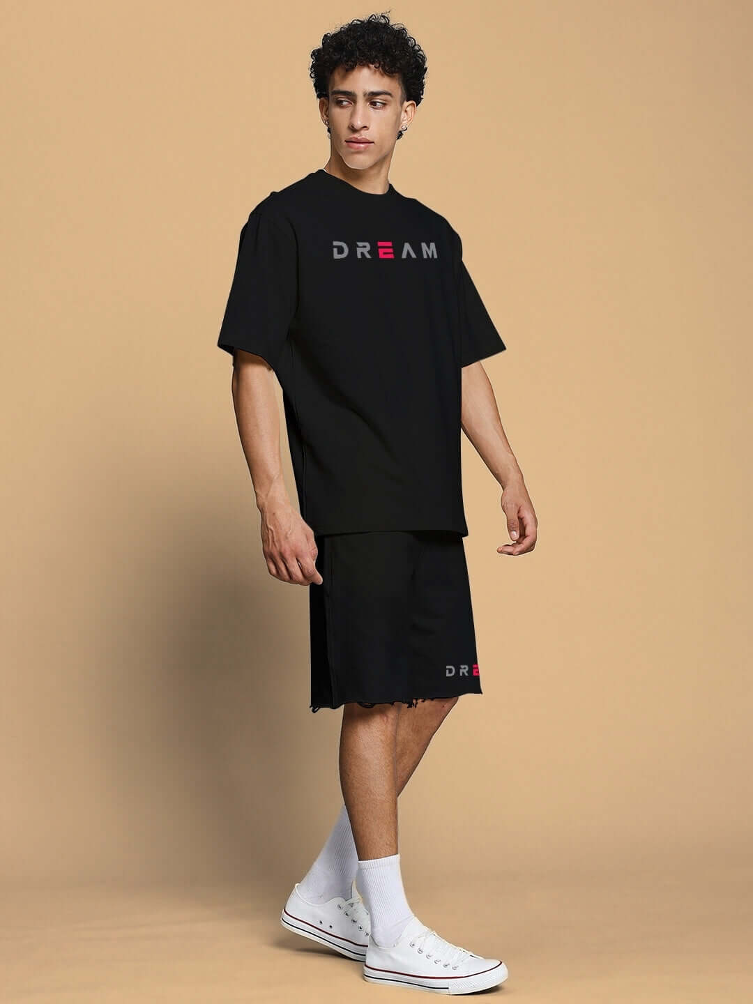 Person wearing FANCY DREAM REGULAR FIT SHORTS BLACK with matching t-shirt, standing against a beige background.