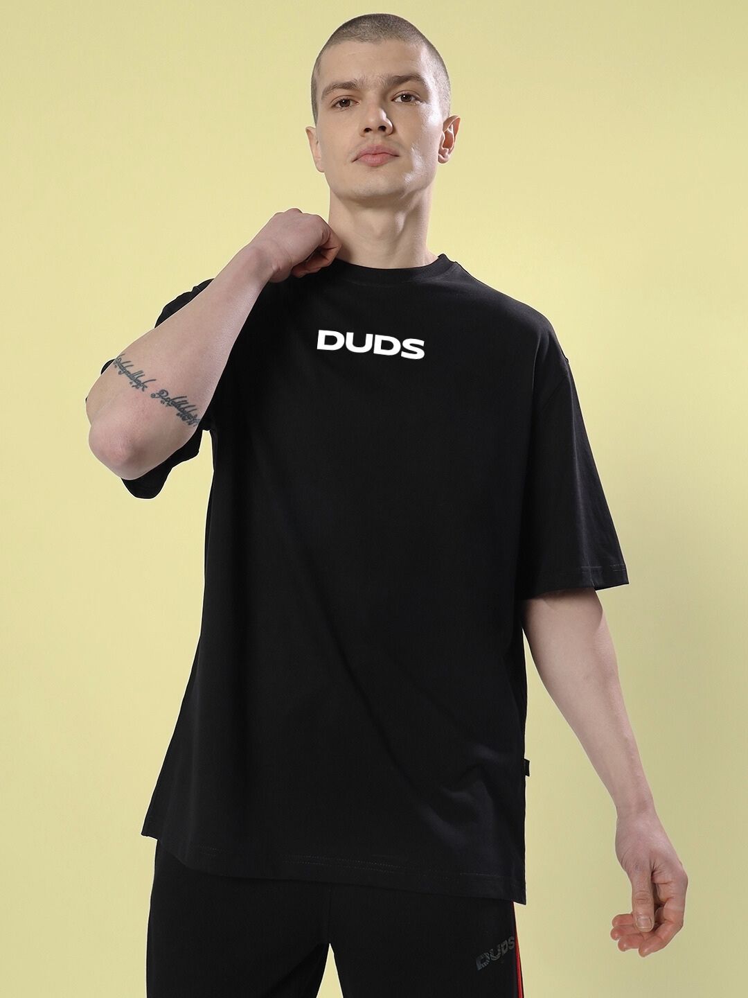 Model wearing a FARARI PRINTED OVERSIZED T-SHIRT BLACK against a yellow background, showcasing casual style.