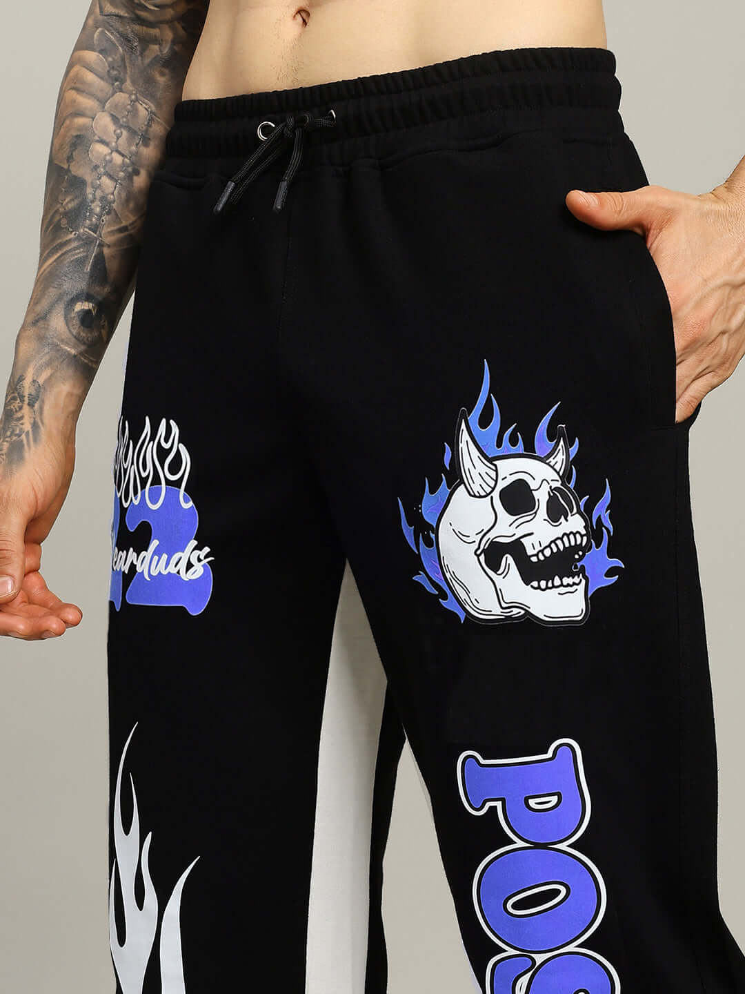 Close-up of black-blue relaxed fit joggers with graphic skull and text art, designed by DUDS, showcasing an edgy style.