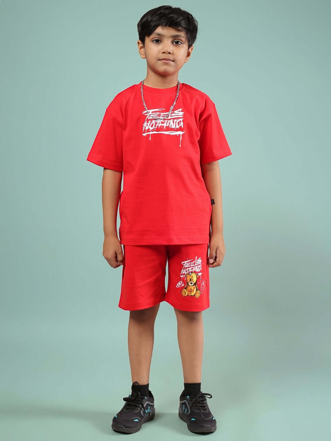 Child wearing red FEELS NOTHING coordinate set by DUDS, featuring a graphic t-shirt and shorts, against a muted background.