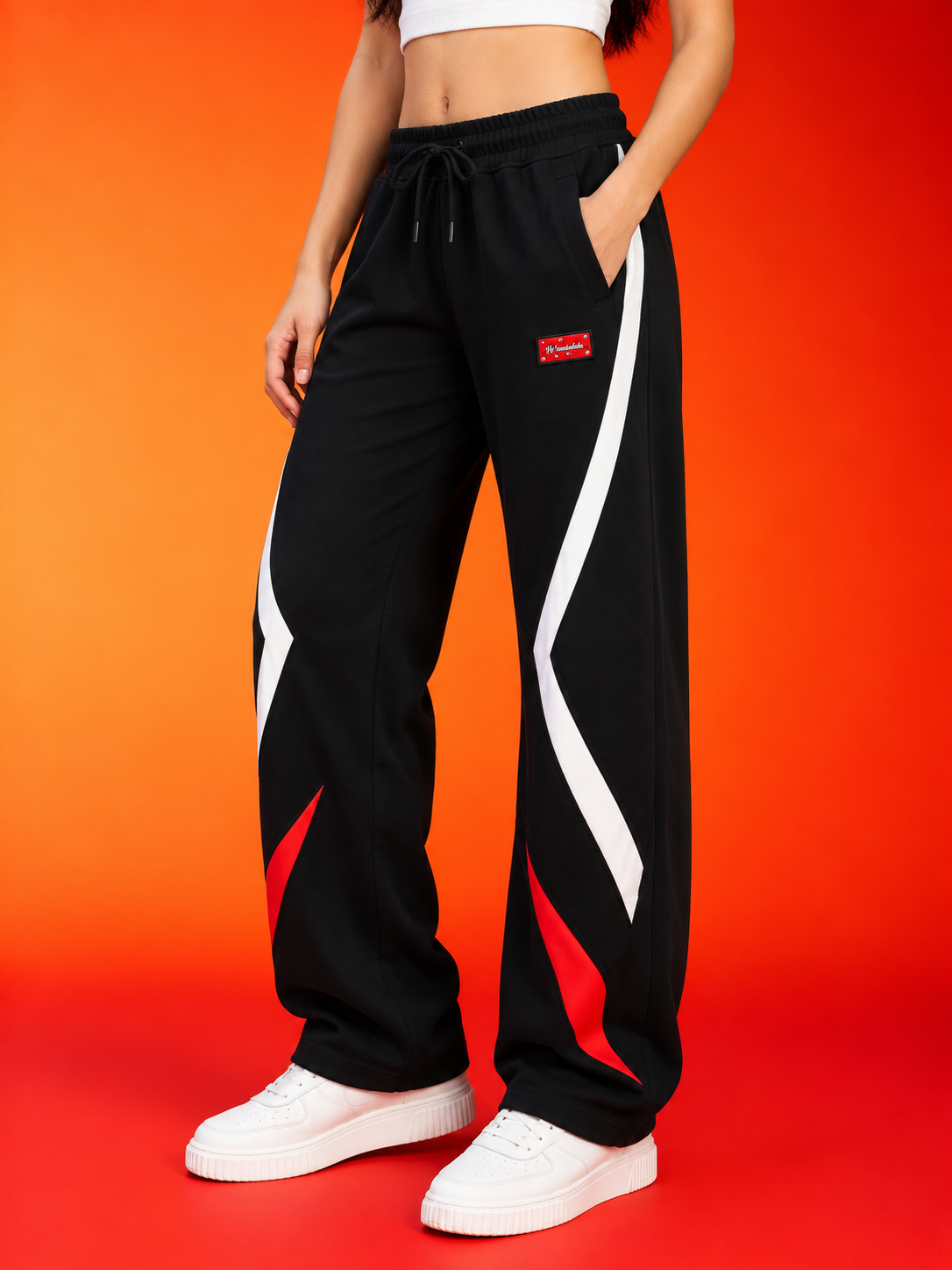 WOMEN METROPOLITAN JOGGERS BLACK WHITE RED STRIPE worn by model against a vibrant orange background.