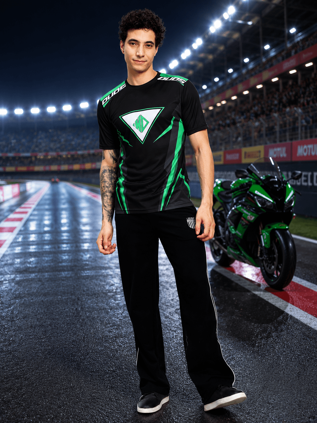 APEX RACING T-SHIRT BLACK worn by a model at a racing track with motorcycle in the background.