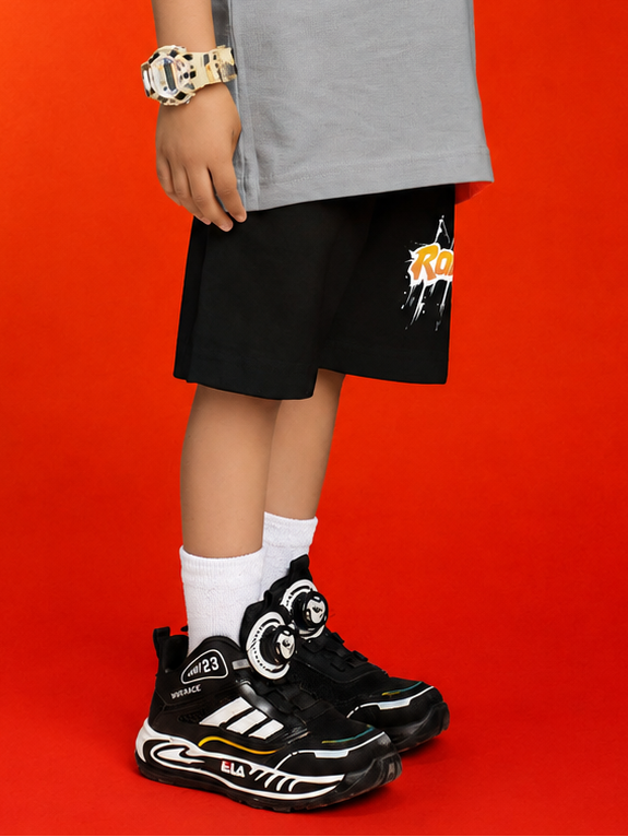 ROBLOX WORLD FIT SHORTS FOR BOYS GIRLS BLACK worn by a kid with stylish sneakers against a bright red background.