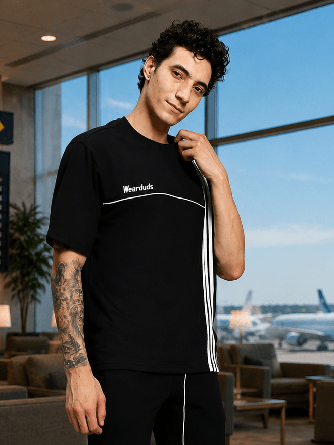 YOUTH CONTREST PIPING T-SHIRT BLACK worn by a model in a stylish airport lounge setting.