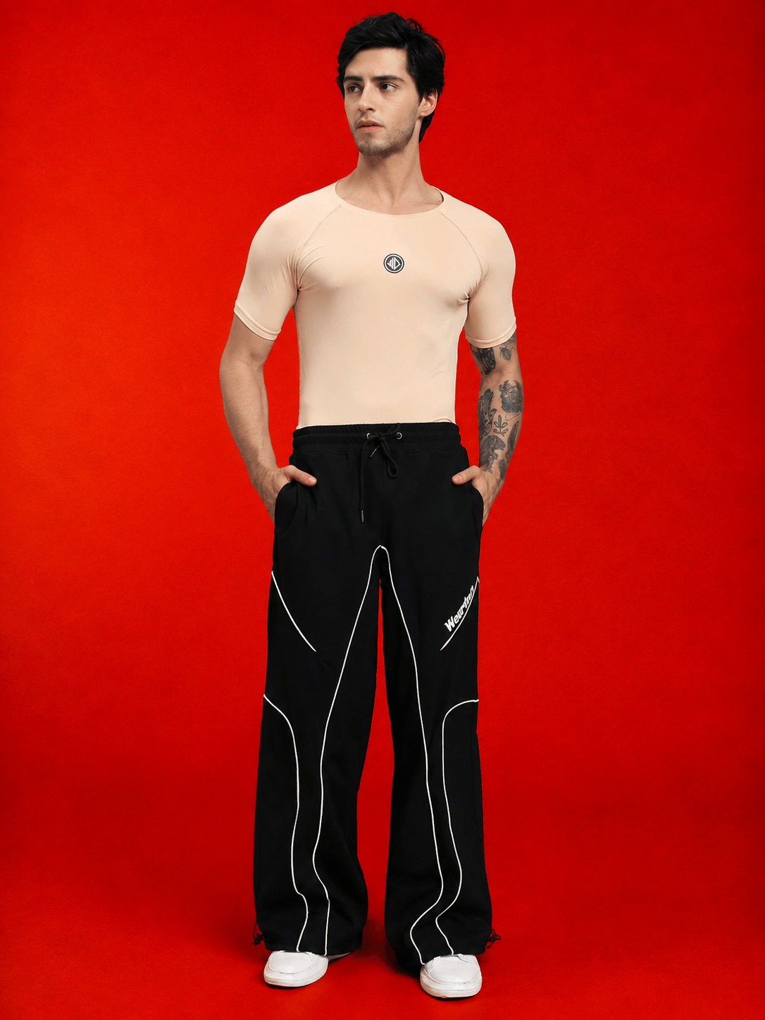 Model wearing SIGNATURE PIPING JOGGERS BLACK featuring contrast piping against a vibrant red background.