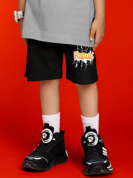 ROBLOX WORLD FIT SHORTS FOR BOYS GIRLS BLACK worn by a child with sporty black sneakers on a red background.