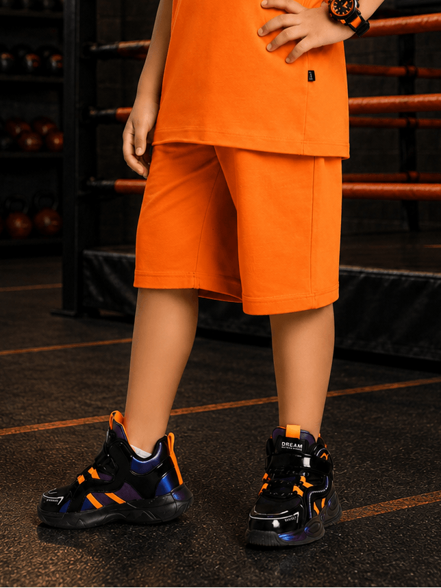 NEON RUSH SHORTS FOR BOYS GIRLS ORANGE worn by a child in a sporty setting, paired with stylish sneakers.