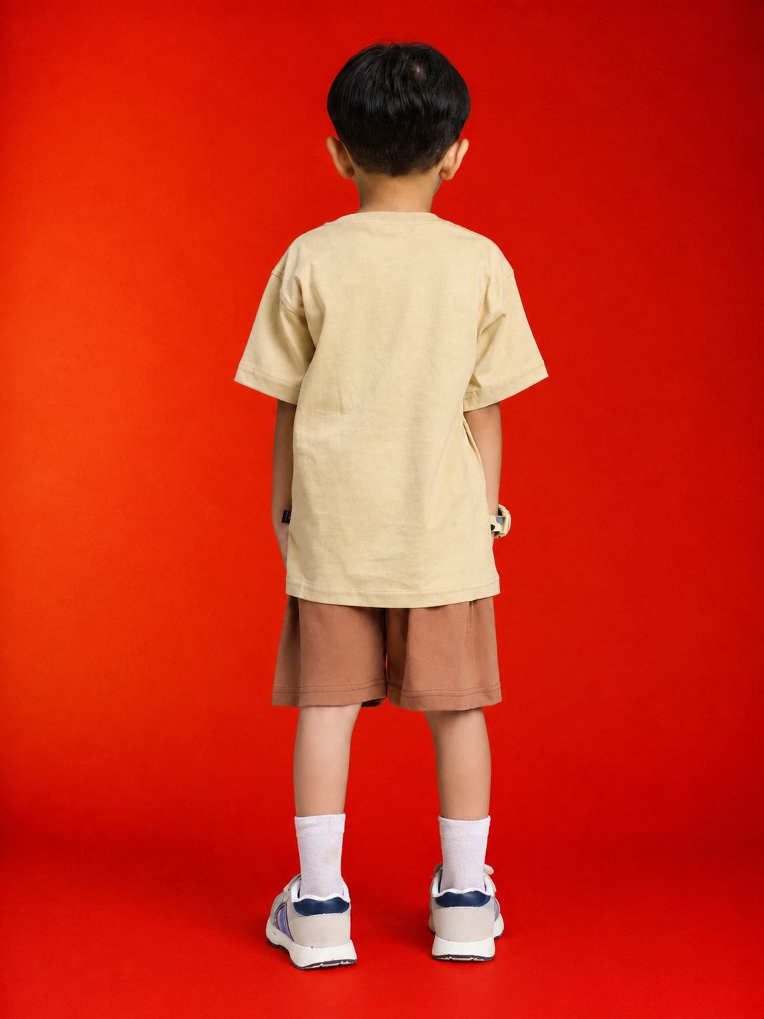 Boy wearing LITTLE EXPLORER TEDDY CO-ORD FOR BOYS GIRLS BEIGE BROWN, showing the back view against a red background.