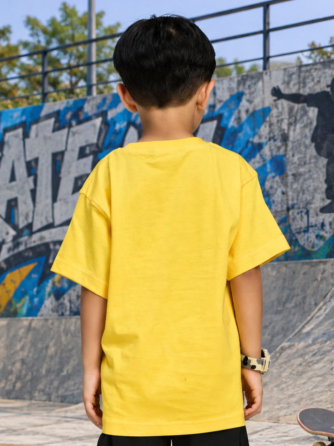Back view of a child wearing a bright yellow COOL DUDE SKATER T-SHIRT FOR BOYS GIRLS YELLOW in a skatepark setting.
