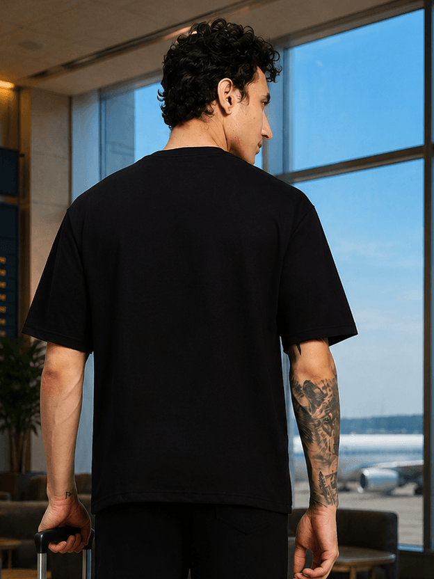 YOUTH CONTREST PIPING T-SHIRT BLACK worn by a man, showcasing the back view in an airport setting.