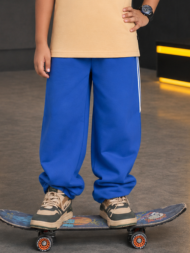 NEO STREET DROP JOGGER FOR BOYS GIRLS BLUE worn by a child standing on a skateboard, showcasing vibrant color and style.
