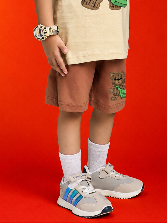 LITTLE EXPLORER TEDDY SHORTS FOR BOYS GIRLS BROWN worn by a child, featuring a teddy bear design, against a vibrant background.