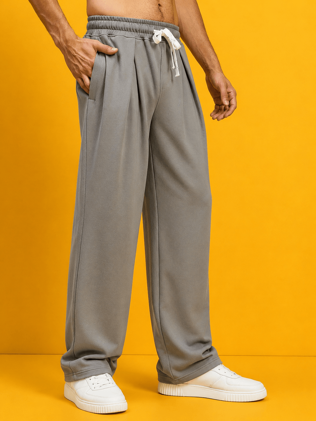 Man wearing DRAPE TAILORED FIT JOGGERS GREY paired with white sneakers on a bright yellow background.