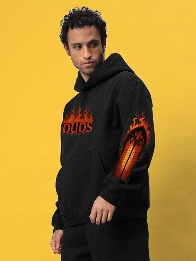 Model wearing FIRE NEVER KILLS THE LIGHT PRINTED FLEECE HOODIE BLACK with flame graphics and bold streetwear design.