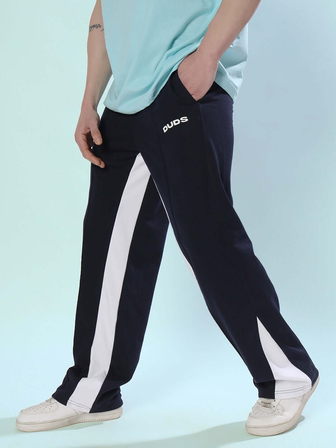 Man wearing navy blue floppy flared contrast joggers by DUDS, featuring white side stripes and casual sneakers.