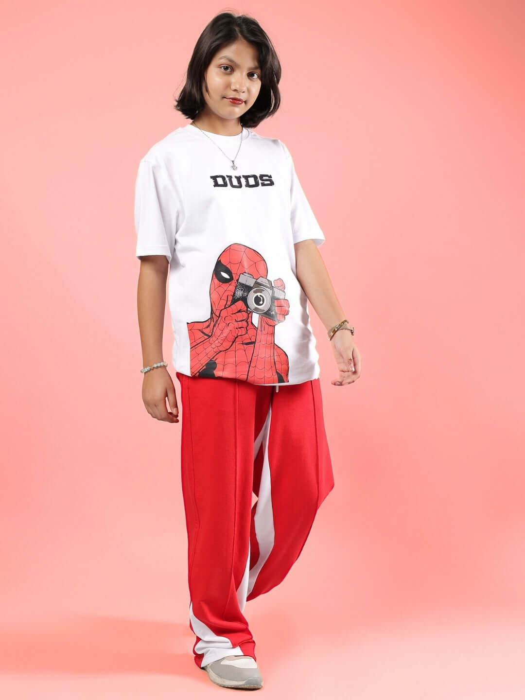 Child wearing red floppy jogger pants and a graphic white t-shirt by DUDS on a pink background.