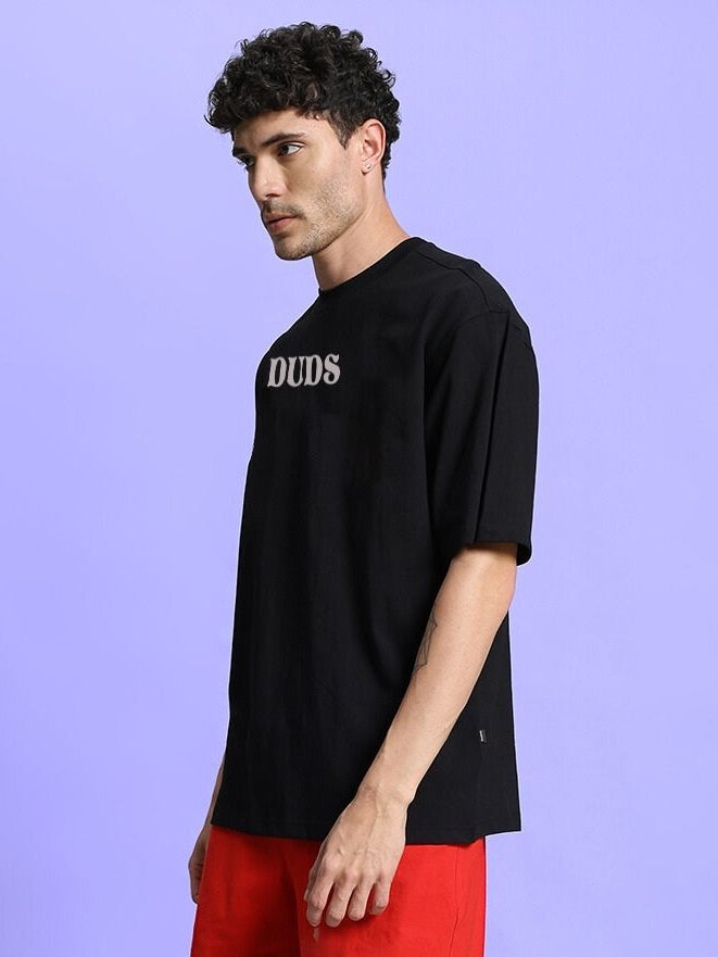 Man wearing a black FLORAL PRINT OVERSIZED T-SHIRT BLACK with a side view, showcasing casual style against a purple background.