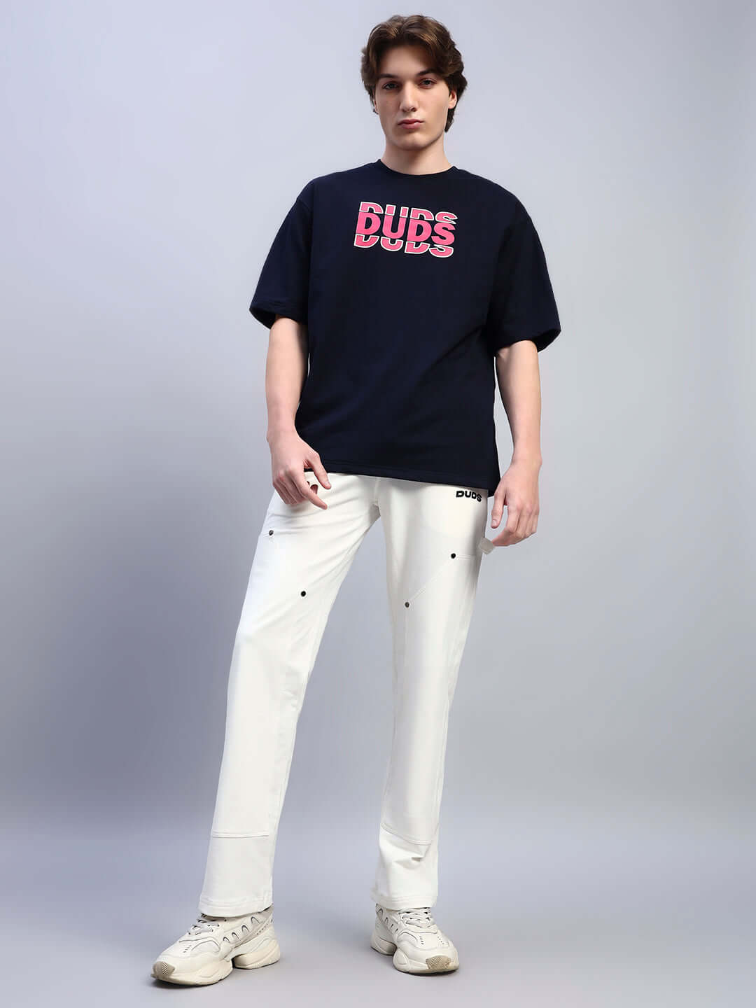 Man wearing FLORES CREATIVE PRINT OVERSIZED T-SHIRT NAVY BLUE with stylish white pants and sneakers.