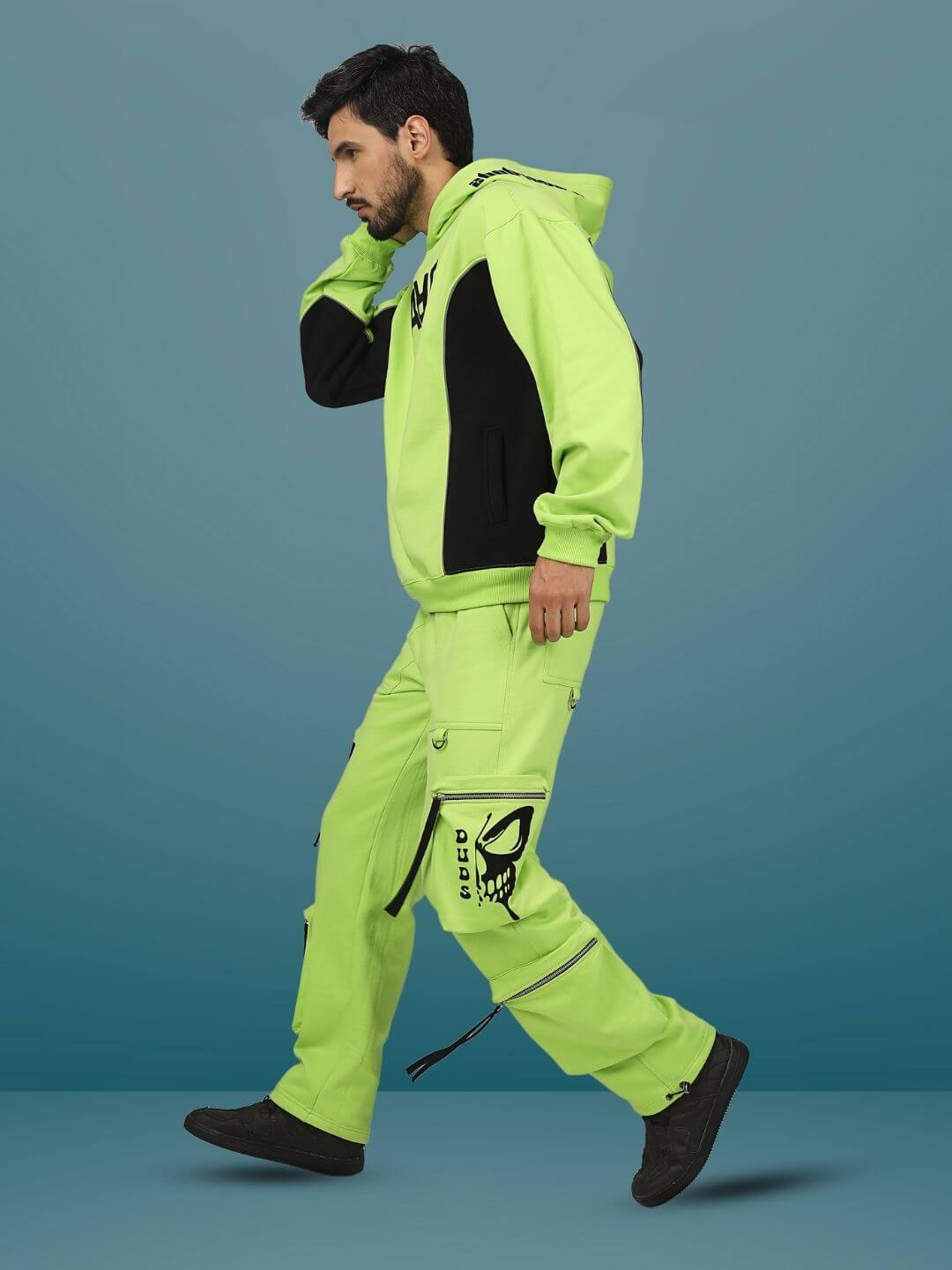 Person wearing fluorescent neon green multi-pocket cargo pants with black accents, standing against a teal background.