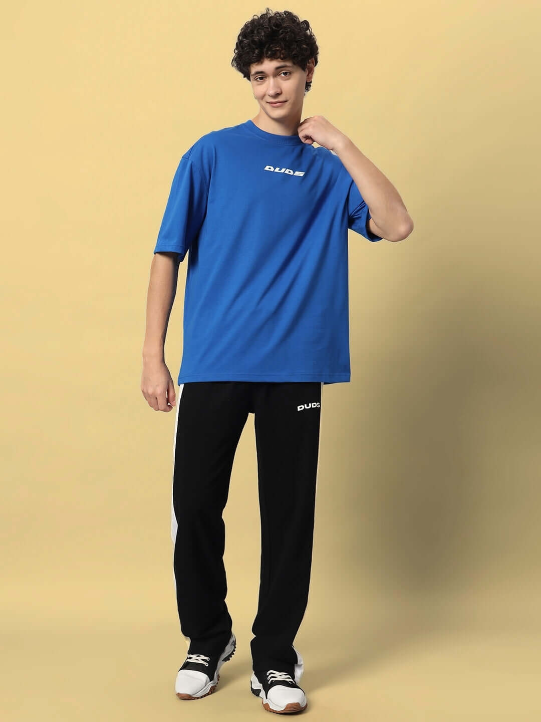Man wearing FLURRY CONTRAST JOGGERS in black and white, paired with a blue DUDS t-shirt, standing on a beige background.