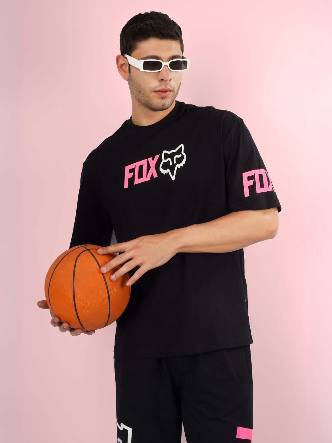 Model wearing FOX oversized black t-shirt with pink logo, holding a basketball, showcasing custom fit options for fashion-forward look.