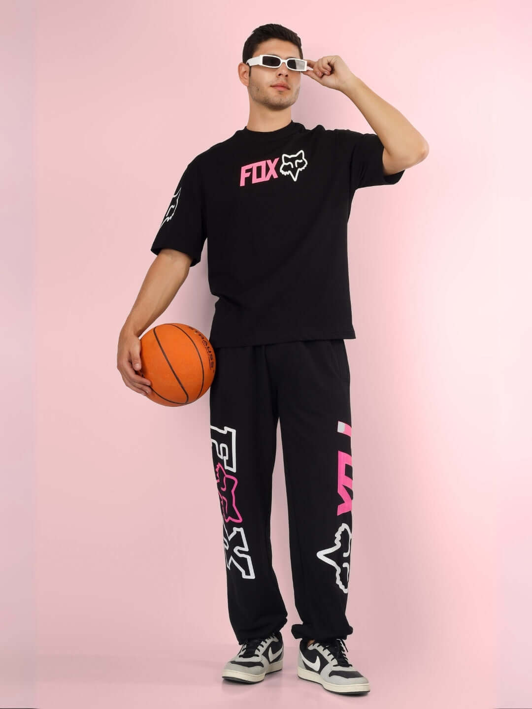 Model wearing black FOX oversized t-shirt holding basketball, showcasing custom fit option in stylish sportswear with pink accents.