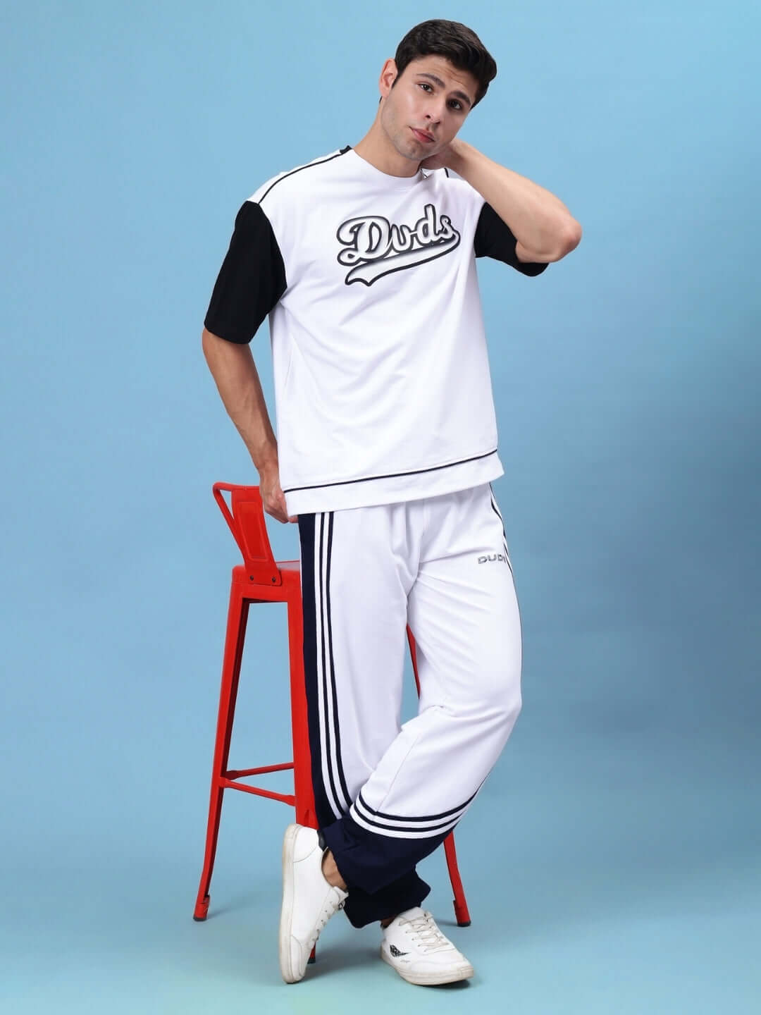Man wearing Frenzy Curve Contrast Joggers in white-navy with DUDS logo, standing by a red chair, showcasing sporty casual style.