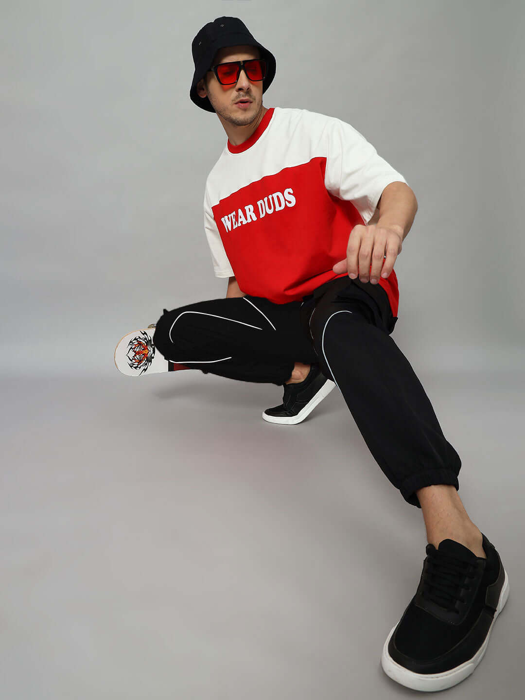 Model wearing FRONTLINE REFLECTOR PARACHUTE CARGO PANT BLACK with red and white shirt and bucket hat, showcasing urban street style.