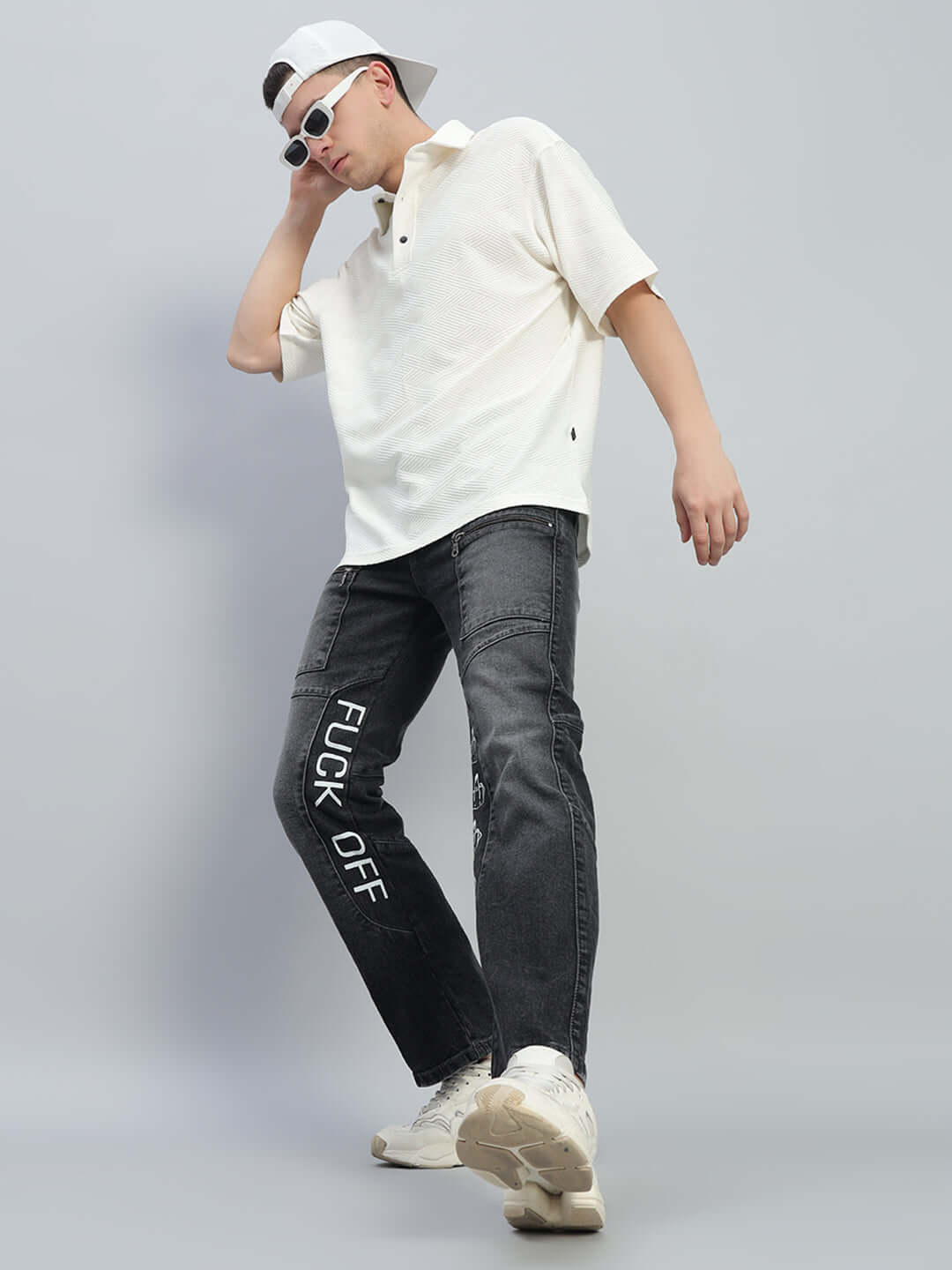 Model wearing black regular fit denim jeans with 'FUCK OFF' text, paired with a casual white shirt and sneakers.