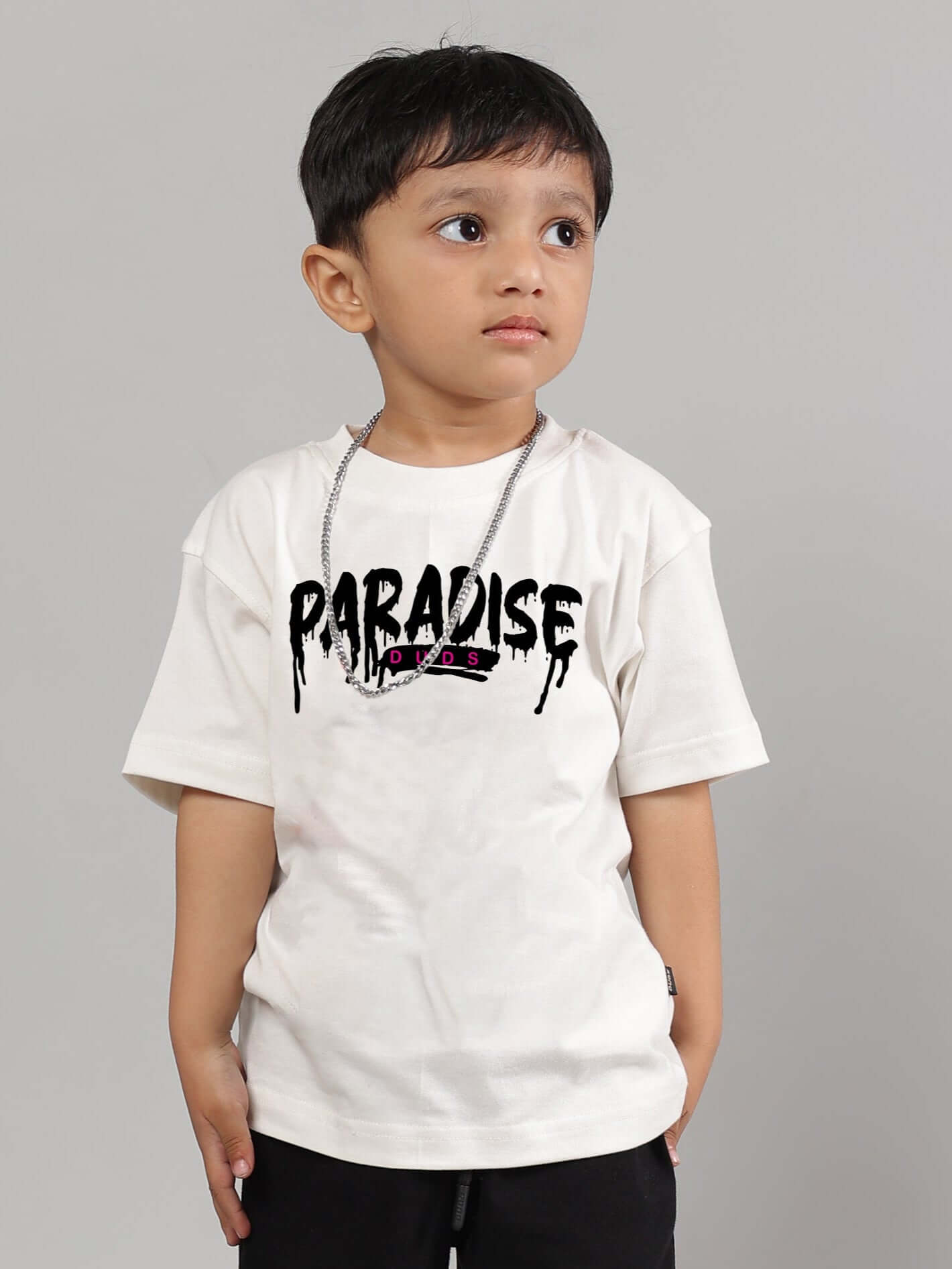 Young child wearing an off-white "FULNESS PARADISE" t-shirt for boys and girls, showcasing casual style.