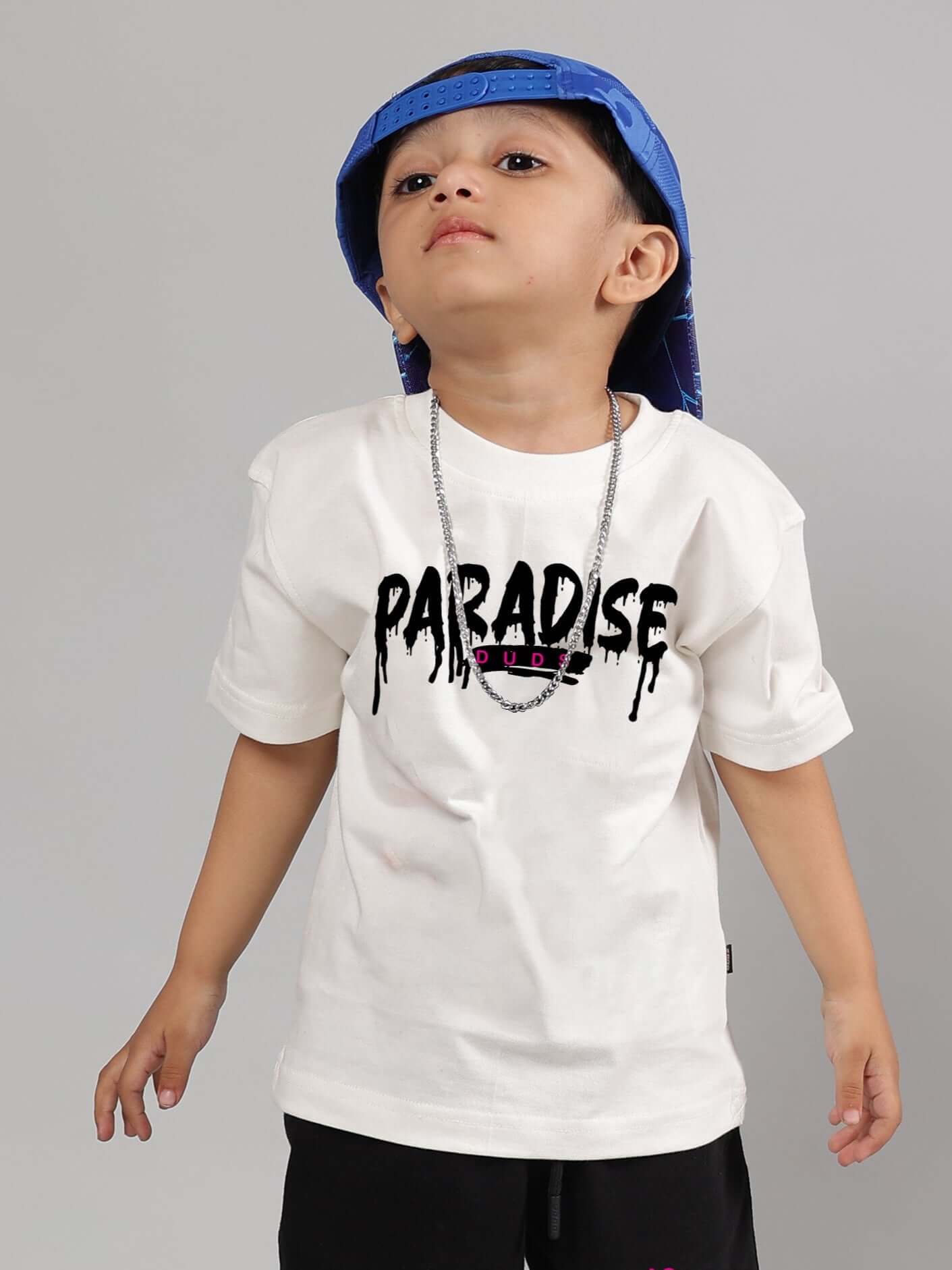 Boy wearing a Fulness Paradise off-white t-shirt and blue cap, featuring casual style by DUDS.