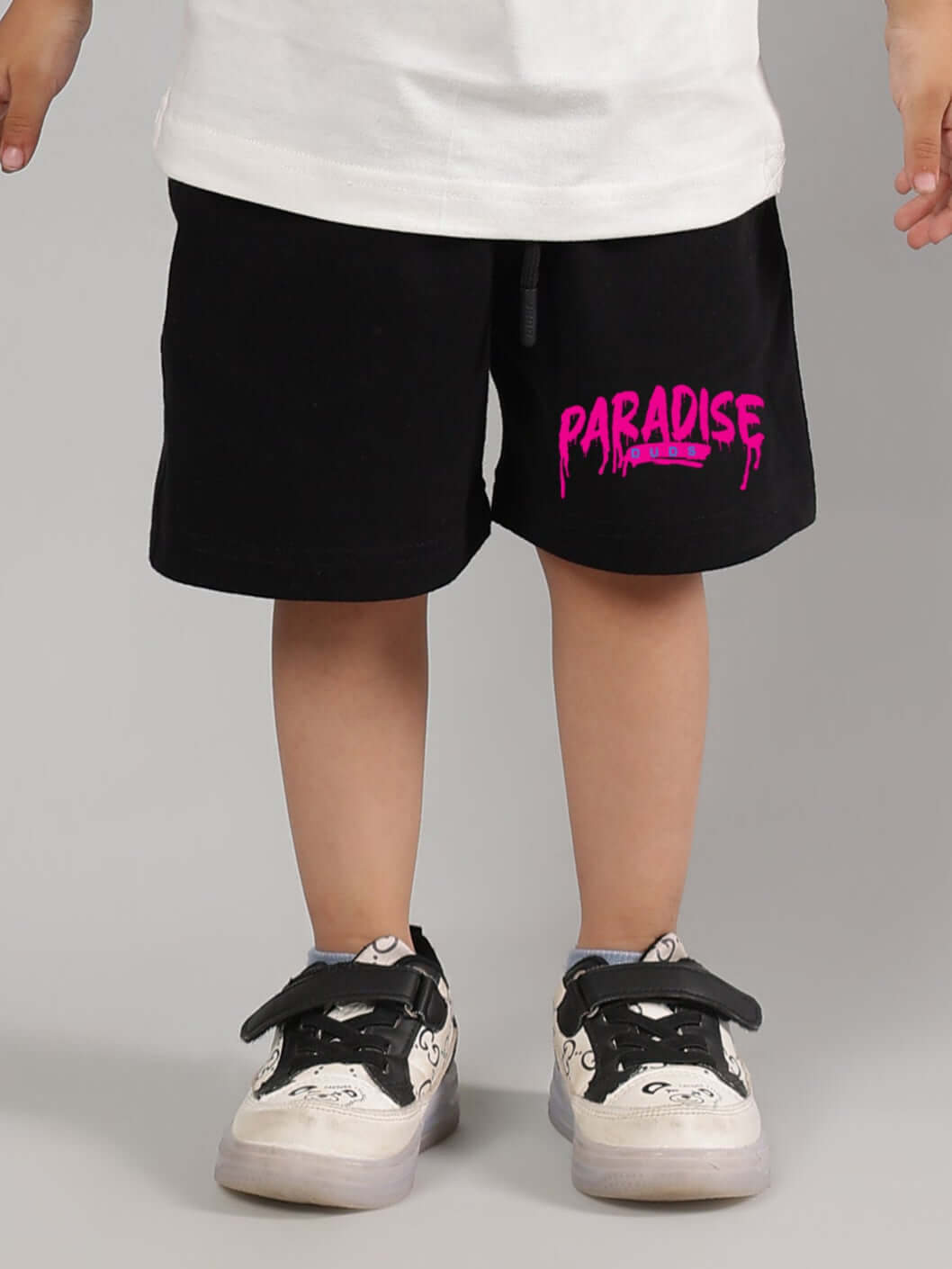 Black summer shorts for kids with "PARADISE" printed in pink, paired with casual sneakers, designed for boys and girls.