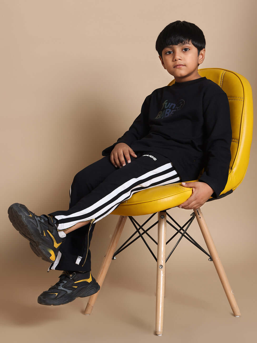 Young child wearing black Fun Babe Co-Ord set for boys and girls, sitting on a yellow chair; stylish kids' fashion.