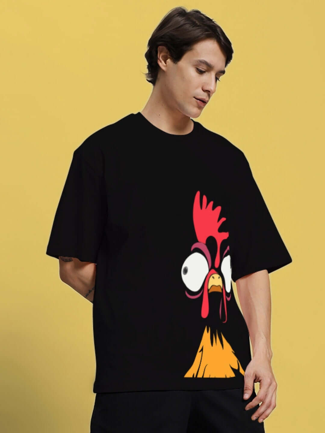 Man wearing a FUNNY CHICKEN PRINTED OVERSIZED T-SHIRT BLACK with quirky chicken graphic on a yellow background.