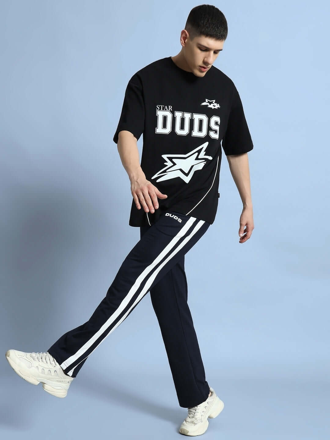 Model wearing FUTURE ICON 2 STRIPE JOGGER in navy blue with a black DUDS t-shirt against a blue background.