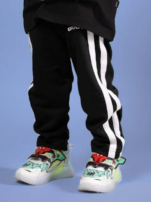 Boy wearing FUTURE ICON JOGGER FOR BOYS & GIRLS BLACK with white stripes and colorful sneakers.