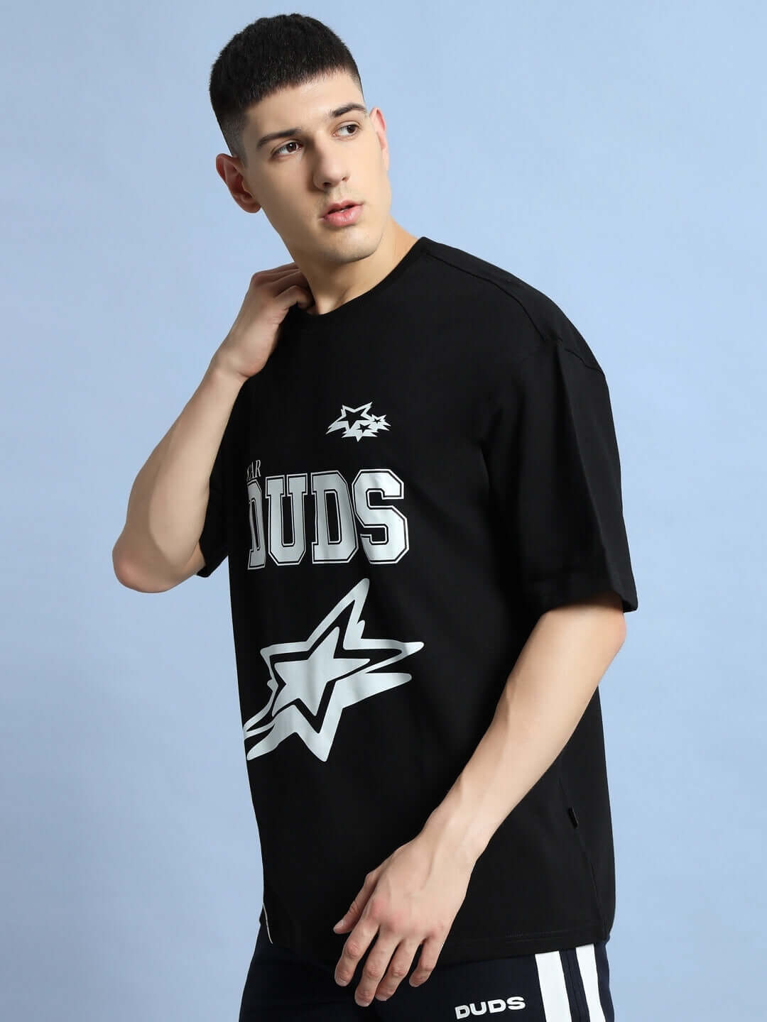 Model wearing black oversized Galaxy T-shirt by DUDS with star design, showcasing casual style against a light blue background.