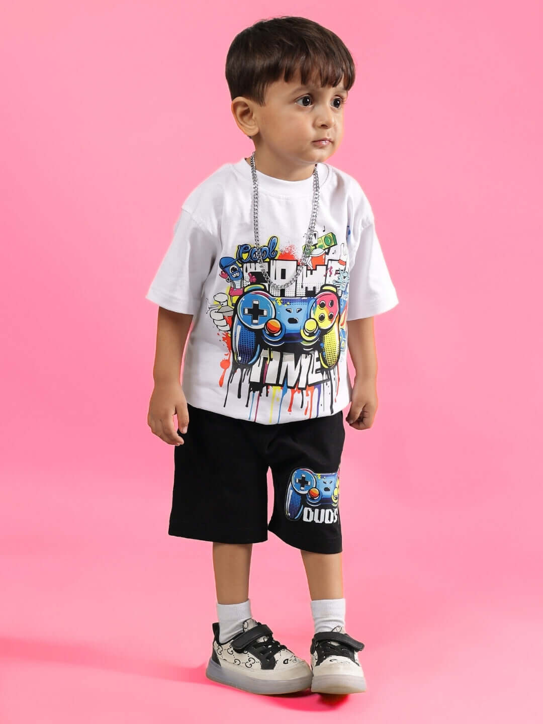 Young child wearing DUDS Game Time Co-ord in white and black, featuring colorful game controller graphics on a pink background.