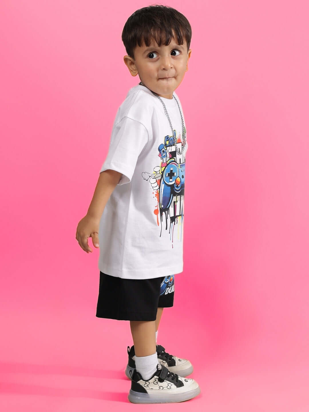 Child wearing Game Time Shorts for Boys & Girls in black with graphic tee against a pink background.