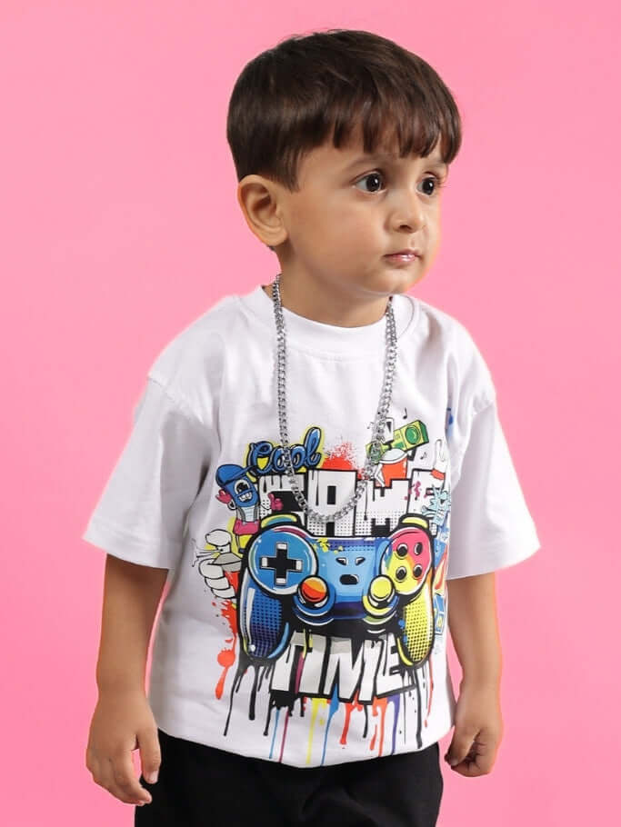 Young boy wearing Game Time T-Shirt for boys girls white with a graphic design, standing against a pink background.