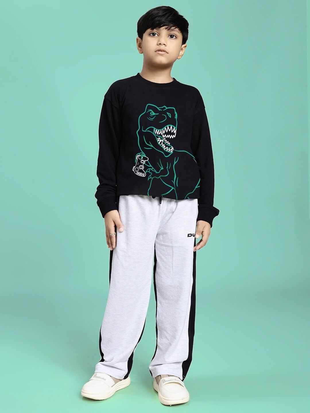Child wearing GAMEING REX PRINT SWEATSHIRT FOR BOYS GIRLS BLACK with dinosaur graphic, paired with casual pants against a green background.