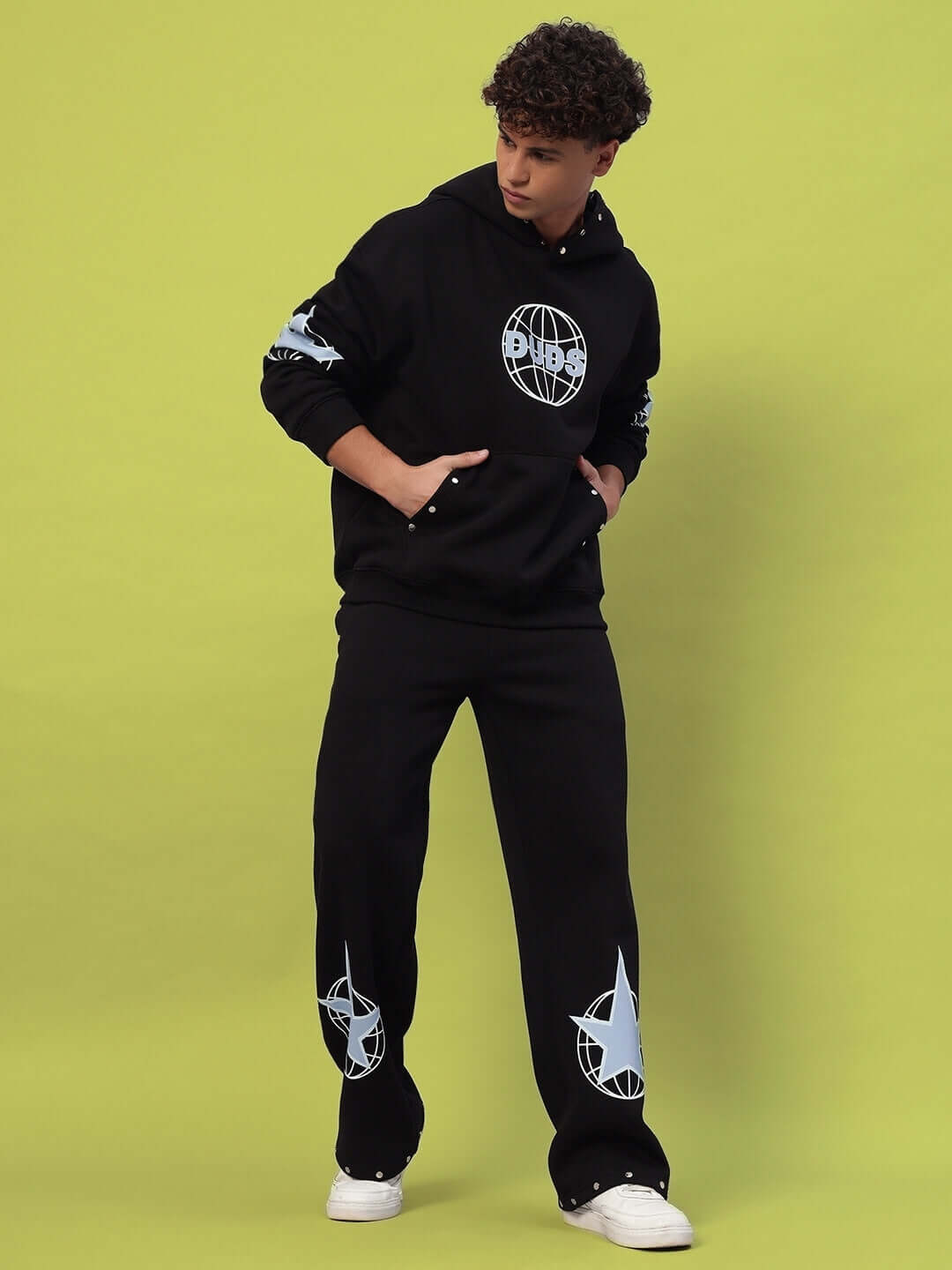 Person wearing a black Global Cotton Fleece Jogger set with graphic designs, standing against a green background.