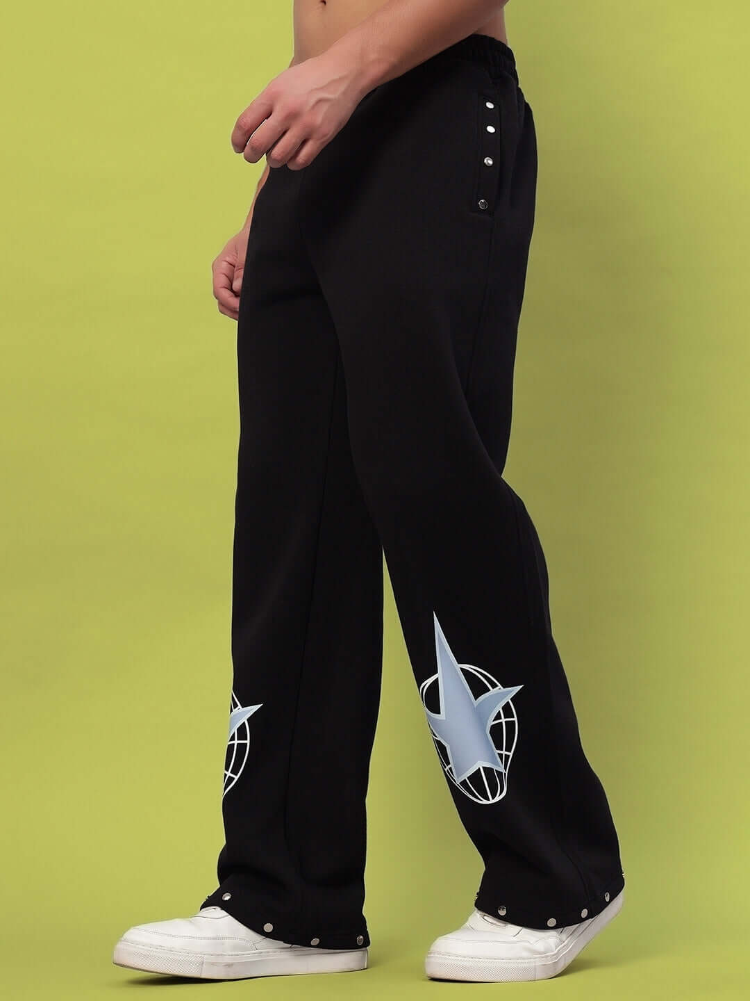 Black fleece joggers with side embellishments and graphic design, modeled with white sneakers against a lime green background.