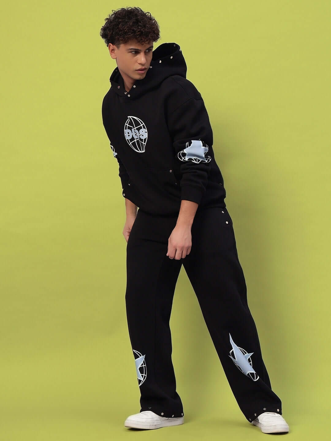 GLOBAL COTTON FLEECE CO-ORD BLACK streetwear set with hoodie and joggers against a green background, featuring urban design elements.