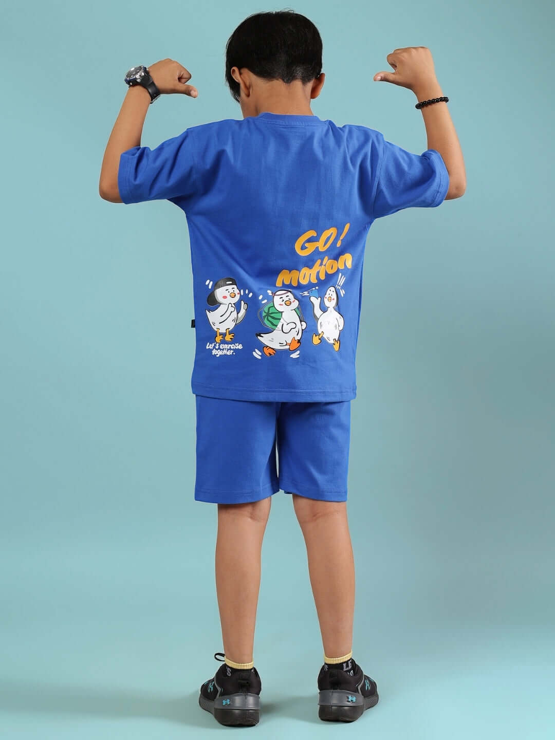 Young boy wearing a blue GO MOTION co-ord set for boys and girls featuring playful graphics on the back, standing with arms flexed.