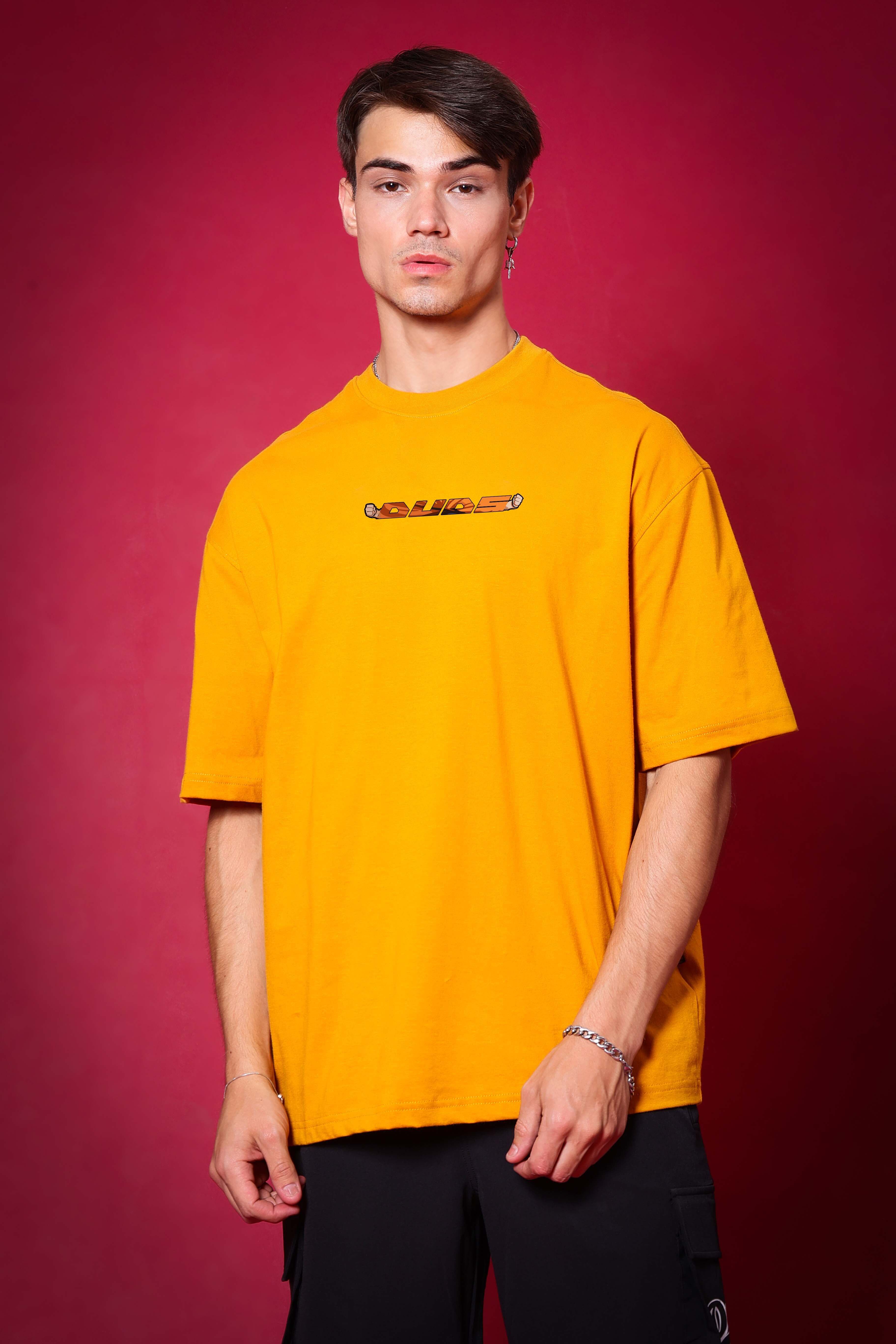 Model wearing GOHAN mustard oversized t-shirt against a red background, showcasing casual and trendy fashion from DUDS.